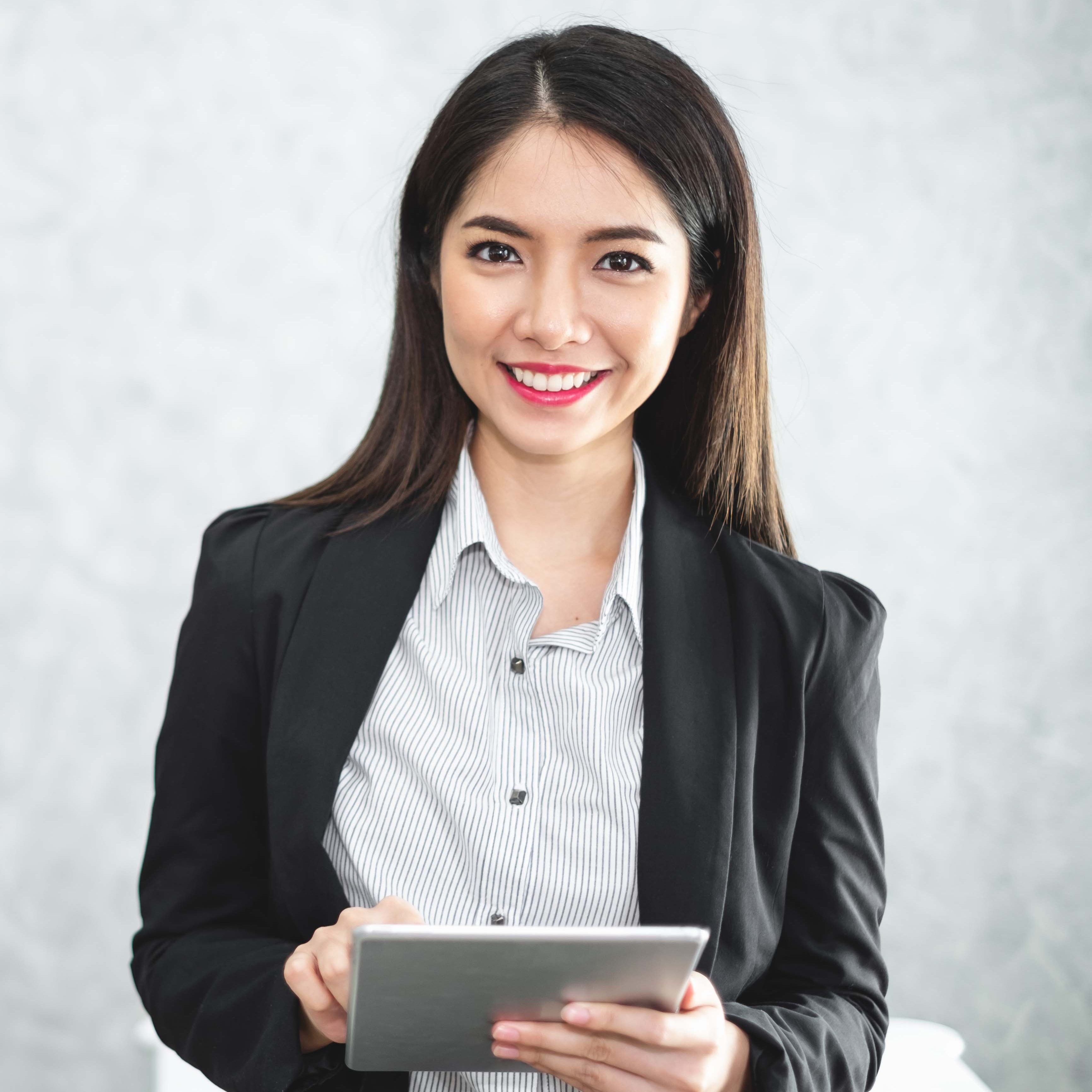 Portrait young Asian businesswoman holding tablet/smartphone in formal suit in office with copy space